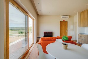 A modern living room with a large window, a television, orange furniture, and a dining area.
