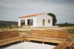 A white building with a red roof, large windows, and a wooden bench in the foreground.