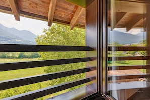 Ein Zimmer mit Blick auf Berge und Grünflächen durch große Fenster mit horizontalen Jalousien.