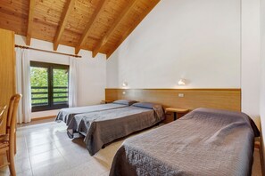A room with two beds, wooden ceiling beams, a window with curtains, and a wooden nightstand. - Apartment 'Casa Serena&Giacomo 9' with Mountain View, Shared Garden and Wi-Fi (Bezzecca)
