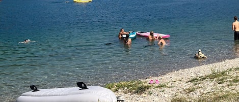 Un lago con barcos, gente nadando y una orilla cubierta de hierba.