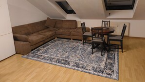 A loft-style room with a brown sectional sofa, a dining table with chairs, a patterned rug, and a skylight.