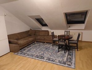 A loft-style room with a brown sectional sofa, a dining table with chairs, a patterned rug, and a skylight.