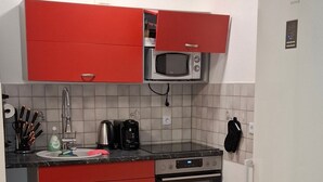 A compact kitchen with red cabinets, a microwave, a kettle, and a stove.