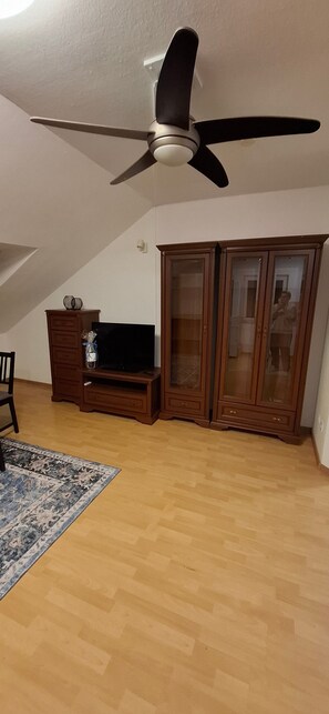 Ein Zimmer mit Deckenventilator, Holzschränken, einem Fernseher auf einem Schrank und einem gemusterten Teppich.
