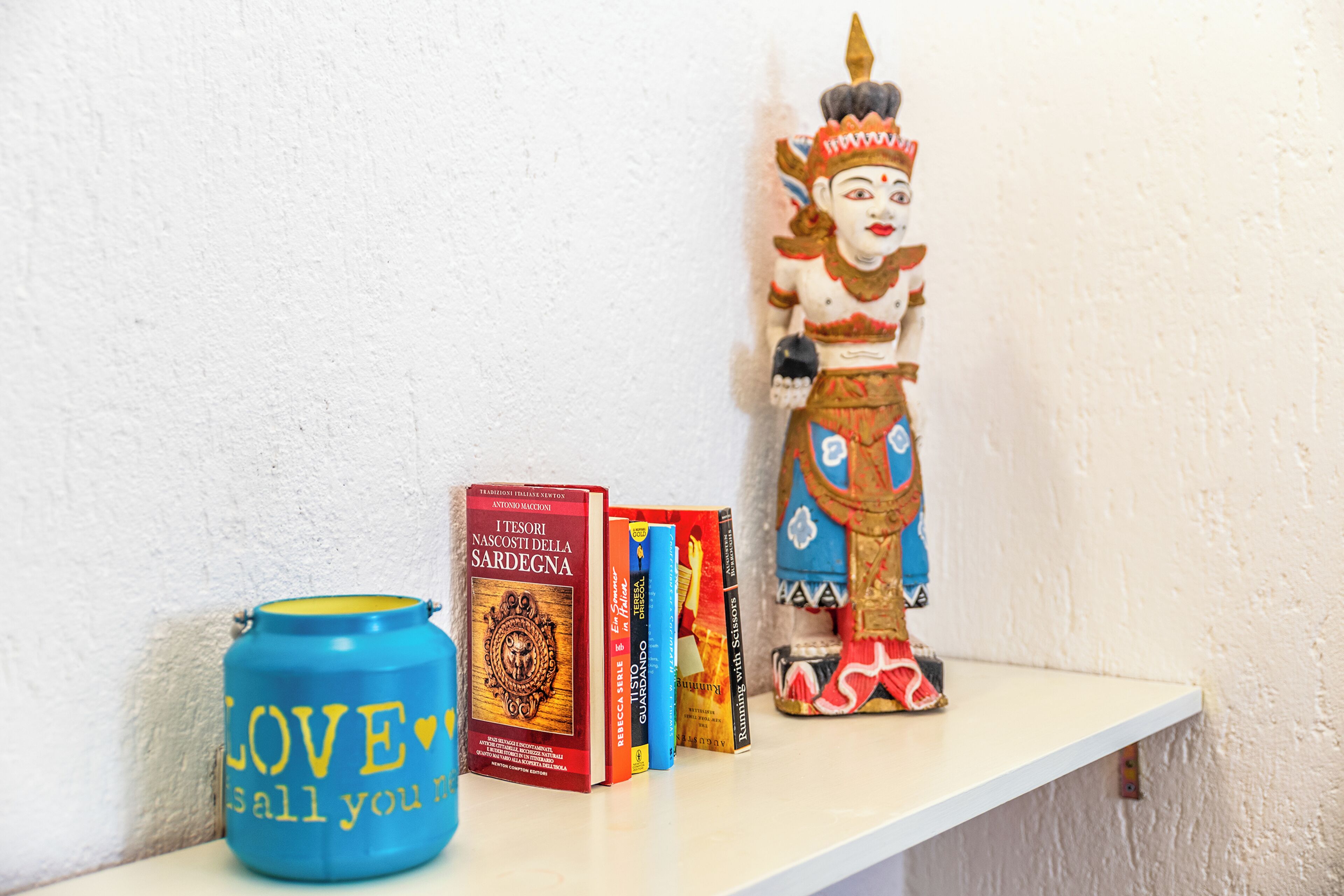 Una estantería con libros, un adorno y un recipiente azul con texto.