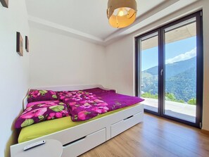 Quarto com cama, porta de correr de vidro, luminária no teto e vista para montanhas.