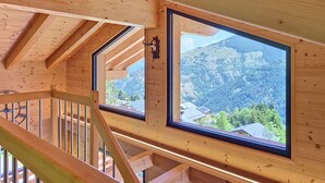 Ein Holzinterieur mit Blick auf eine gebirgige Landschaft durch ein großes Fenster.