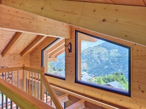 Ein Holzinterieur mit Blick auf eine gebirgige Landschaft durch ein großes Fenster.