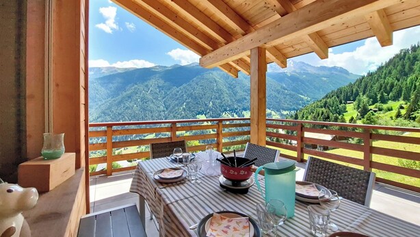 Eine Holzdiele mit Esstisch, mit Blick auf eine gebirgige Landschaft.