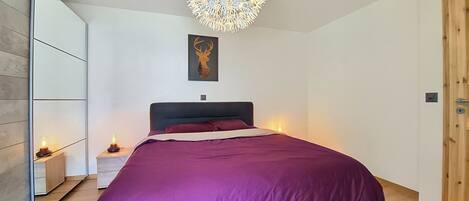 A bedroom with a bed, a wall-mounted light fixture, a framed deer head artwork, and a wooden door.