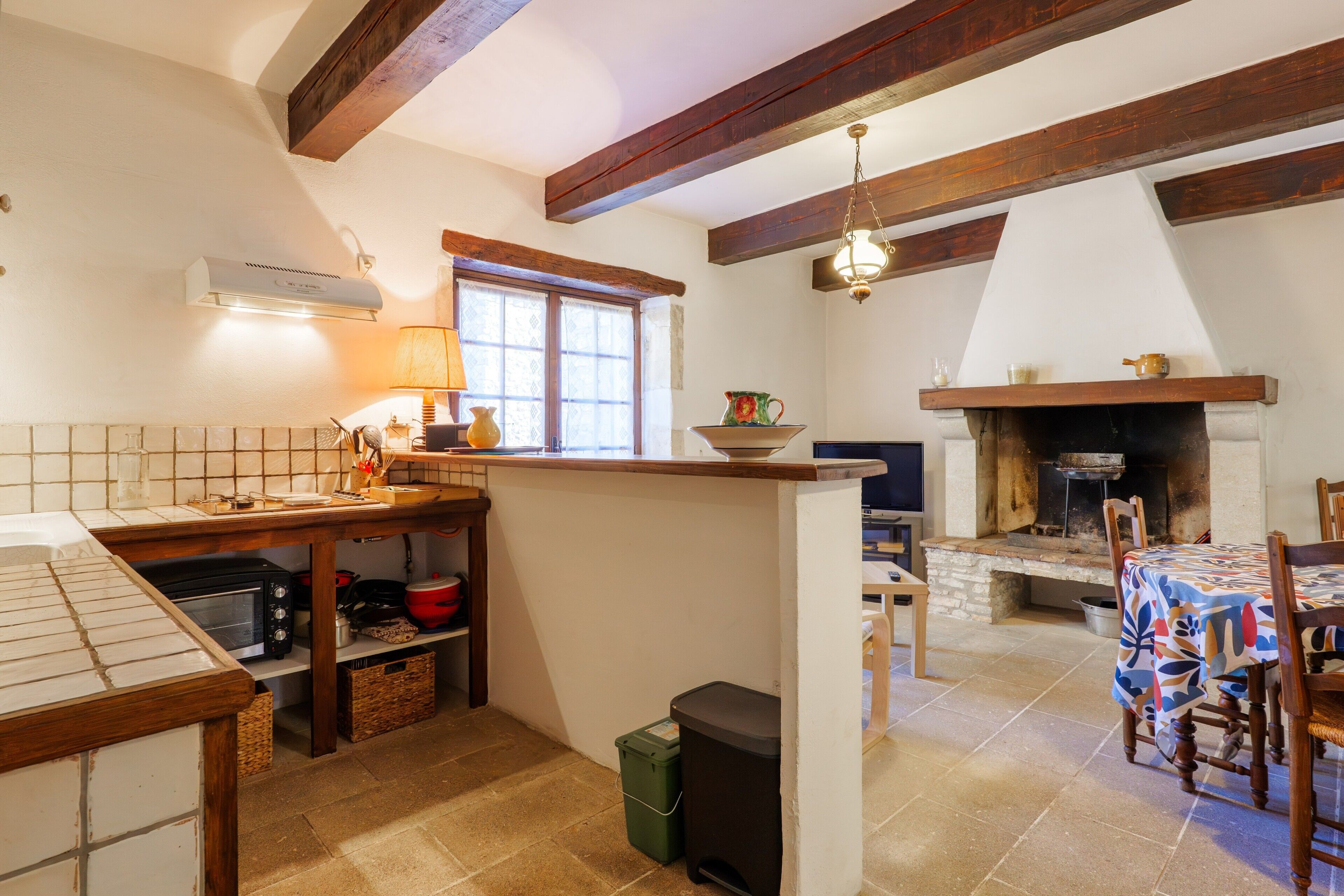 Una cocina con salpicadero de azulejos, vigas de madera, una ventana, una chimenea y un comedor con mesa y sillas.