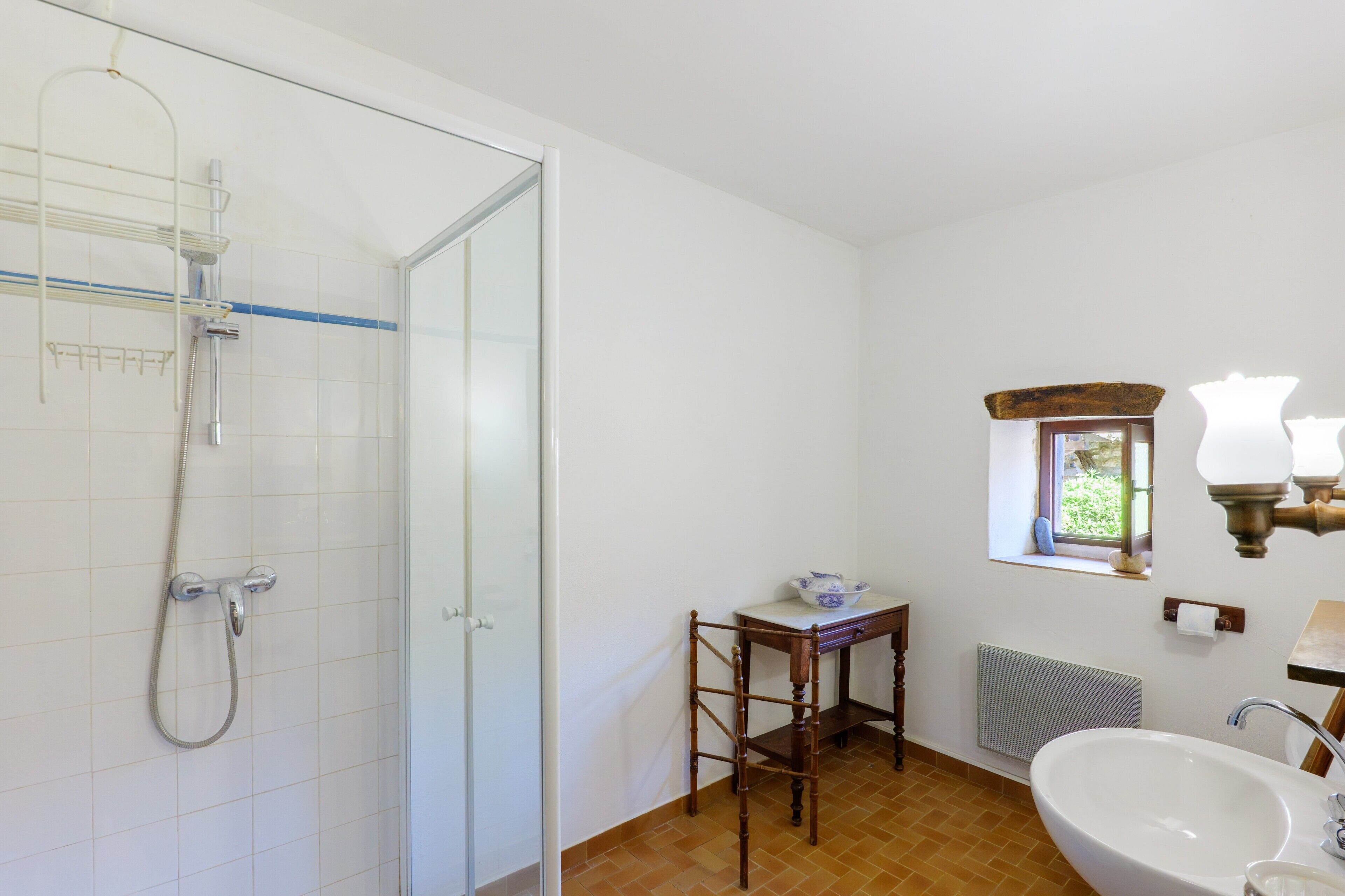Ein Badezimmer mit Duschkabine aus Glas, einem hölzernen Stuhl, einem Waschbecken und einem Fenster mit Aussicht.