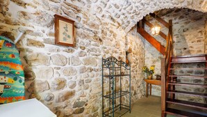 A stone-walled room with a metal rack, a wooden staircase, and a framed picture on the wall.