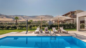 A swimming pool with lounge chairs and umbrellas, surrounded by greenery and a view of hills. - Orama Sunset | Ammi Villa (Rhodes)