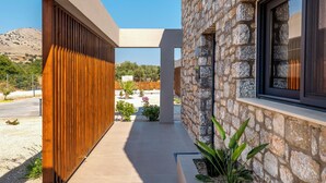 A modern building with a stone facade, a wooden slatted wall, and a tiled pathway. - Orama Sunset | Ammi Villa (Rhodes)