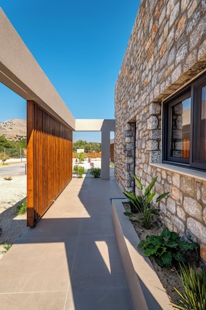 A modern building with a stone facade, a wooden slatted wall, and a tiled pathway. - Orama Sunset | Ammi Villa (Rhodes)