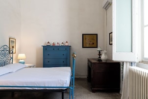 Un dormitorio con cama, cómoda, mesita de noche, lámpara, cuadro enmarcado y ventana con persianas.