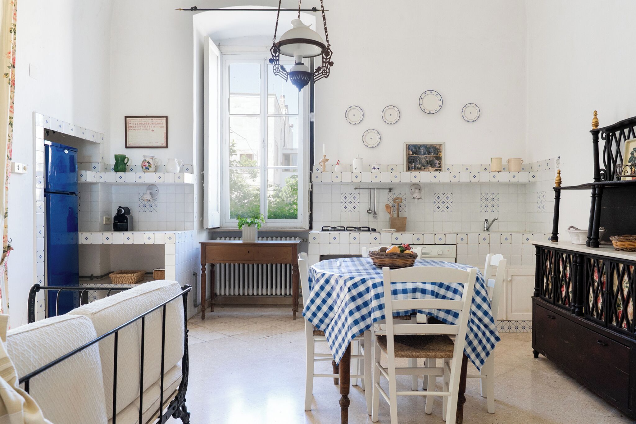 Een keuken met een eettafel, stoelen, een blauwe koelkast en een raam.