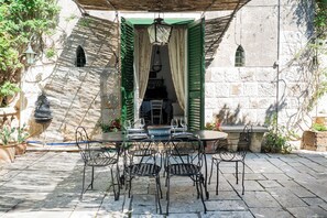 Eine Terrasse im Freien mit einem runden Tisch, Stühlen, einer hängenden Laterne und Blick auf ein Steinhaus.