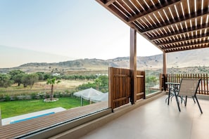 A covered outdoor area with a table and chairs, a view of a landscaped garden, and a distant mountain range. - Orama Sunset | Emily Villa (Rhodes)