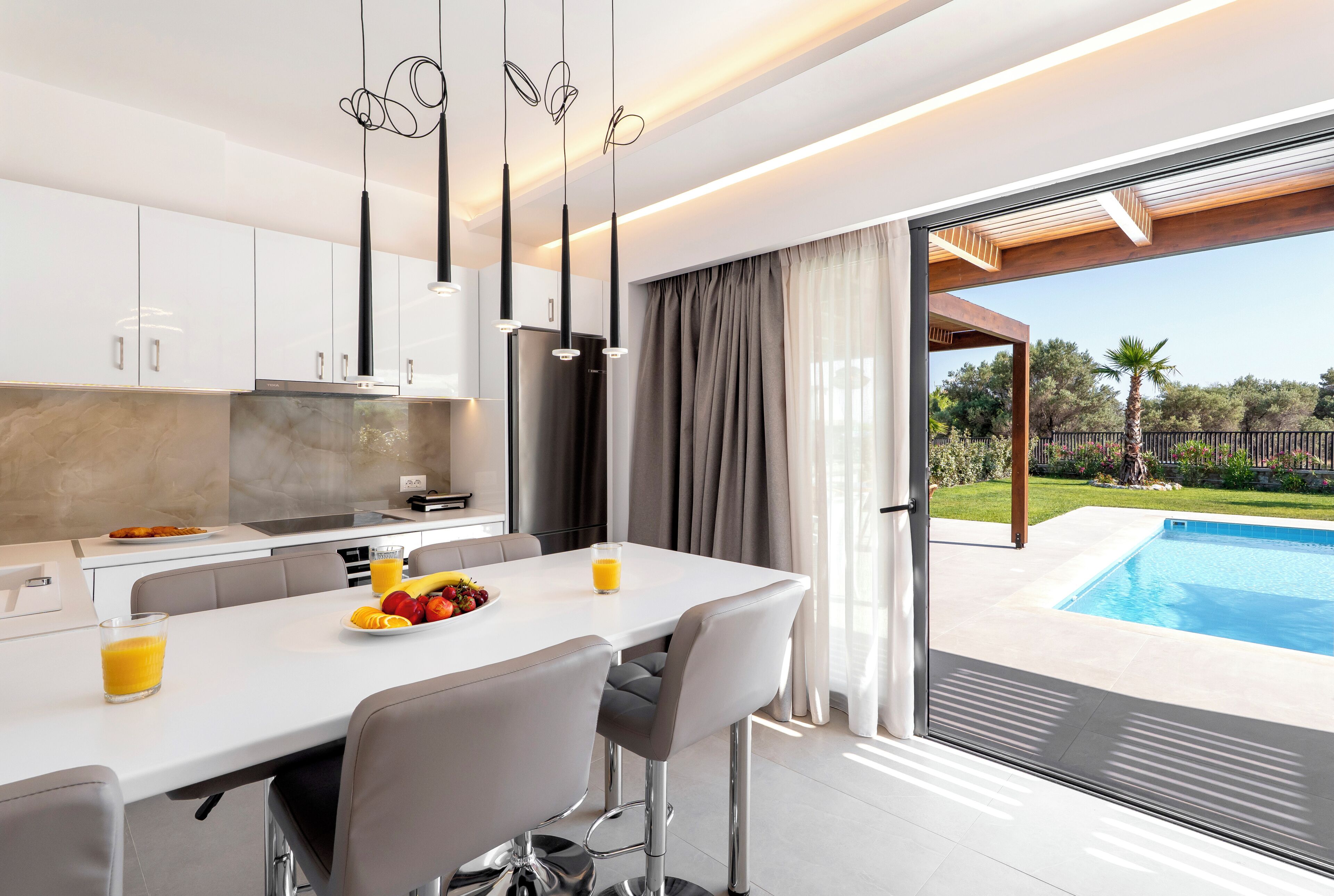 Une cuisine moderne avec des meubles blancs, un coin repas comprenant une table et des chaises, et une vue sur une piscine.