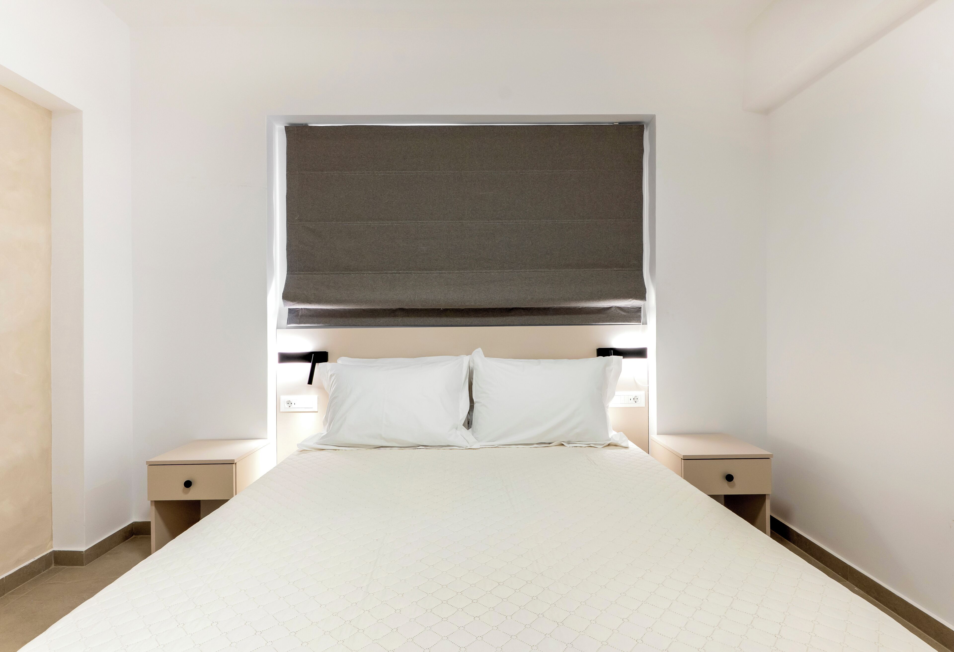 Une chambre à coucher comprenant un lit, deux tables de chevet, une tête de lit et une fenêtre avec un store.