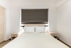 A bedroom with a bed, two bedside tables, a headboard, and a window with a blind. - Orama Sunset | Emily Villa (Rhodes)