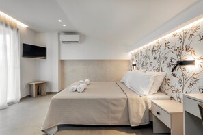 Une chambre d’hôtel moderne équipée d’un lit, d’une table de chevet, d’un téléviseur, d’un climatiseur et d’un mur orné d’un motif floral.