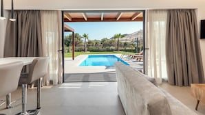 A modern room with a pool, a sofa, a dining area, and a view of the outdoors. - Orama Sunset | Stela Villa (Rhodes)