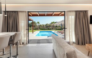 A modern room with a pool, a sofa, a dining area, and a view of the outdoors. - Orama Sunset | Stela Villa (Rhodes)