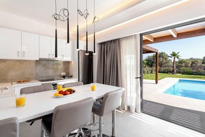 Une cuisine moderne avec des meubles blancs, un coin repas comprenant une table et des chaises, et une vue sur une piscine.