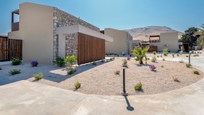 A modern building with a stone facade, a wooden slatted section, and a landscaped garden with gravel and small plants. - Orama Sunset | Stela Villa (Rhodes)