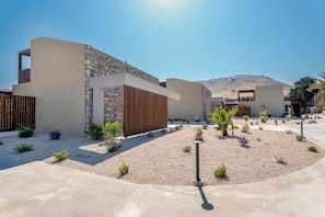 A modern building with a stone facade, a wooden slatted section, and a landscaped garden with gravel and small plants. - Orama Sunset | Stela Villa (Rhodes)