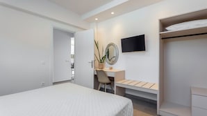 A modern hotel room with a bed, a desk, a chair, a television, and a wardrobe. - Orama Sunset | Stela Villa (Rhodes)