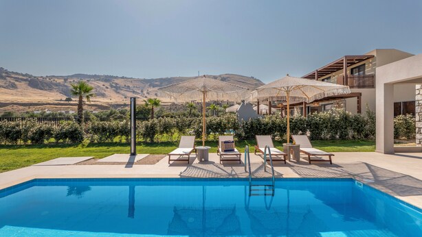A swimming pool with lounge chairs and umbrellas, surrounded by greenery and a view of hills. - Orama Sunset | Joana Villa (Rhodes)