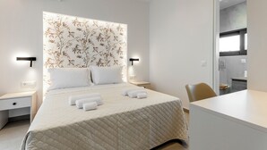 A hotel room with a bed, bedside tables, a chair, and a view into the kitchen. - Orama Sunset | Joana Villa (Rhodes)