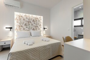 A hotel room with a bed, bedside tables, a chair, and a view into the kitchen. - Orama Sunset | Joana Villa (Rhodes)