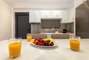 A modern kitchen with white cabinets, a dark door, and a dining table with fruit and juice glasses. - Orama Sunset | Joana Villa (Rhodes)