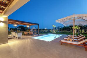 Ein Swimmingpool mit Liegestühlen, einer überdachten Sitzgelegenheit und einer Pergola mit Lichterketten.