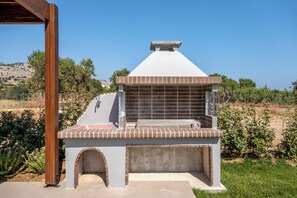 A barbecue grill with a chimney, brick base, and a metal roof. - Orama Sunset | Joana Villa (Rhodes)