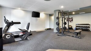 A gym with a treadmill, weight bench, squat rack, and various weights. - Newcastle Views at One Apartments (Newcastle West)