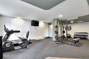 Ein Fitnessraum mit Laufband, einer Hantelbank, einem Squat-Stand und verschiedenen Gewichten.