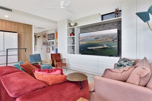 En moderne stue med et stort fladskærms-tv, sofaer med rødt og blåt mønster, og udsigt til bybilledet.