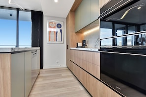 A modern kitchen with wooden cabinets, a black refrigerator, and a countertop with a coffee machine. - Newcastle Views at One Apartments (Newcastle West)