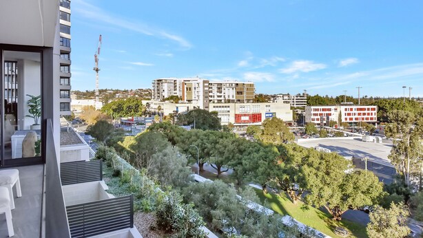 A residential building with multiple floors, a balcony, and a view of a cityscape including a construction crane and various buildings. - Newcastle Views at One Apartments (Newcastle West)