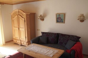 Ein Wohnzimmer mit einer Couch, einem Holzschrank, einem Tisch mit Platzdeckchen und zwei Wandleuchten.