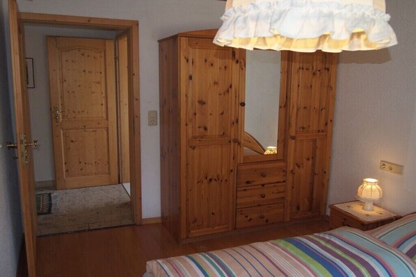 Ein Schlafzimmer mit einem Holzschrank, einem Nachttisch mit Lampe und einer gestreiften Bettdecke.