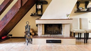 A fireplace with a stone surround, a chair, a shelf with items, and a wooden beam structure.