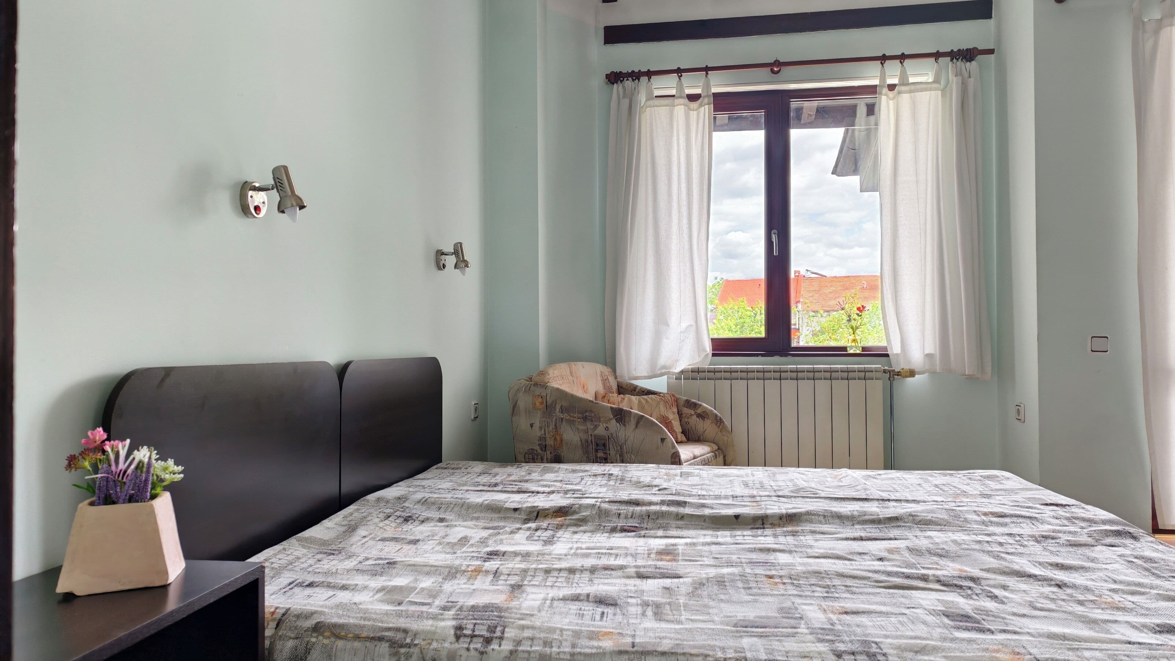 Une chambre à coucher avec un lit, une chaise, une fenêtre avec des rideaux et un radiateur.